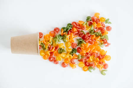 Multicolored pasta in a disposable kraft paper cup scattered on a white background. Top view. Copy, empty space for text.の写真素材