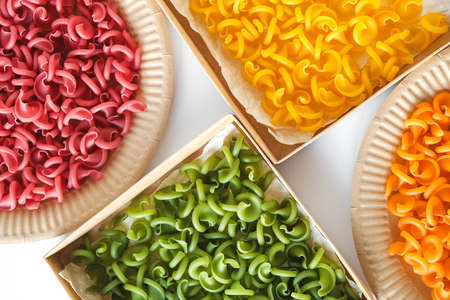 Multicolored pasta in a disposable kraft paper plates and boxes on a white background. Top view. Copy, empty space for text.の写真素材