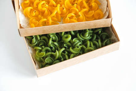 Pasta yellow and green in a cardboard box on a white background. Top view. Copy, empty space for text.の写真素材