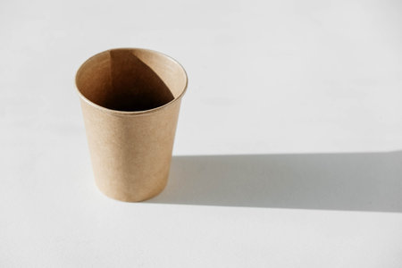 Disposable paper cup with shadow from light on a white background. Copy, empty space for text.