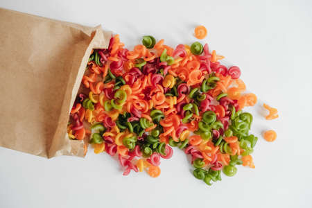 Multicolored pasta in a disposable brown kraft paper paper bag scattered on a white background. Top view. Copy, empty space for text.の写真素材