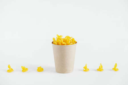 Yellow pasta in a disposable kraft paper cup on a white background. Copy, empty space for text.の写真素材