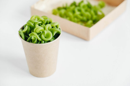 Green pasta in a disposable kraft paper cup on a white background. Copy, empty space for text.の写真素材