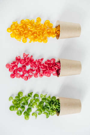 Multicolored pasta in a disposable kraft paper cups scattered on a white background. Top view. Copy, empty space for text.の写真素材
