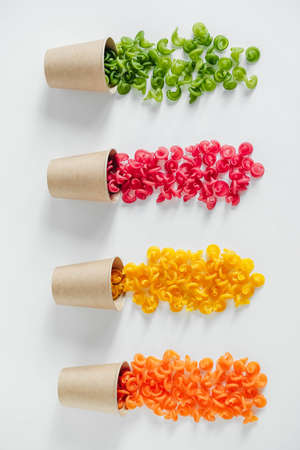 Multicolored pasta in a disposable kraft paper cups scattered on a white background. Top view. Copy, empty space for text.の写真素材