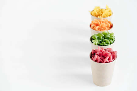Multicolored pasta in a disposable kraft paper cups scattered on a white background. Top view. Copy, empty space for text.の写真素材