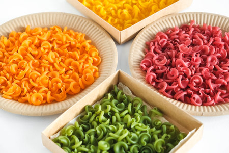 Multicolored pasta in a disposable kraft paper plates and boxes on a white background. Top view. Copy, empty space for text.の写真素材