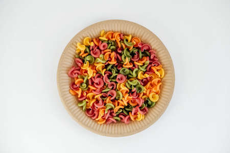 Multicolored pasta in a disposable paper plate on a white background. Top view. Copy, empty space for text.の写真素材