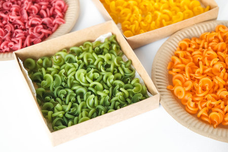 Multicolored pasta in a disposable kraft paper plates and boxes on a white background. Top view. Copy, empty space for text.の写真素材