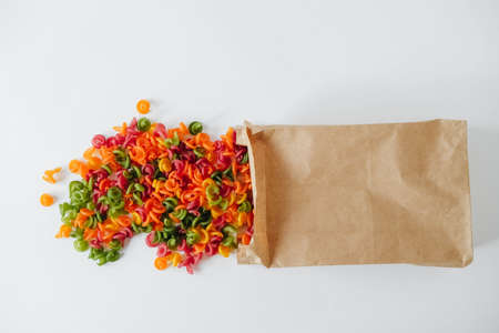 Multicolored pasta in a disposable brown kraft paper paper bag scattered on a white background. Top view. Copy, empty space for text.の写真素材