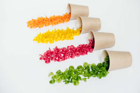 Multicolored pasta in a disposable kraft paper cups scattered on a white background. Top view. Copy, empty space for text.の写真素材