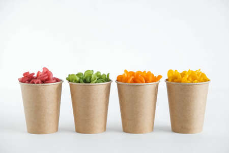 Multicolored pasta in a disposable kraft paper cups scattered on a white background. Copy, empty space for text.の写真素材