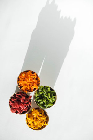 Multicolored pasta in a disposable kraft paper cups scattered on a white background. Top view. Copy,...