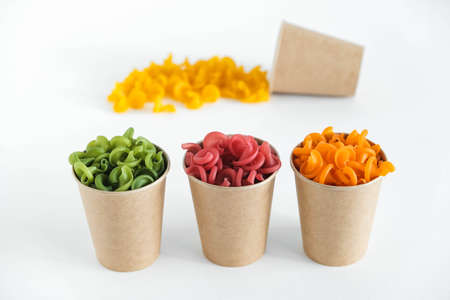 Multicolored pasta in a disposable kraft paper cups scattered on a white background. Copy, empty space for text.の写真素材