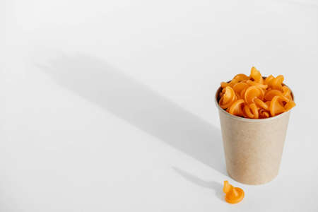 Orange pasta in a disposable kraft paper cup on a white background. Copy, empty space for text.の写真素材
