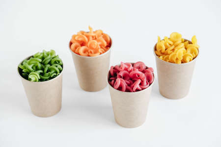 Multicolored pasta in a disposable kraft paper cups scattered on a white background. Top view. Copy, empty space for text.の写真素材