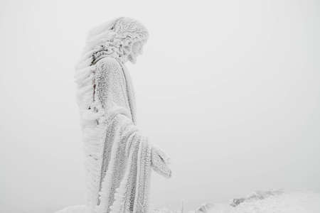 The statue of Jesus is covered with snow and ice on top of the mountain. Copy, empty space for text.の写真素材