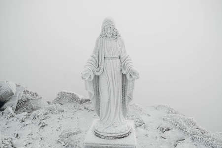 The statue of Jesus is covered with snow and ice on top of the mountain. Copy, empty space for text.の写真素材
