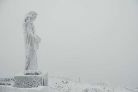 The statue of Jesus is covered with snow and ice on top of the mountain. Copy, empty space for text.の写真素材
