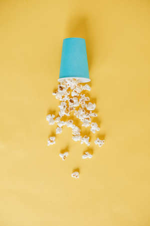 Popcorn in a blue paper cup scattered on a yellow background. Minimalist concept. Top view. Copy, empty space for text.の写真素材