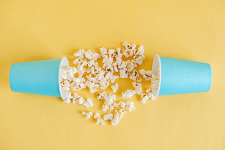 Popcorn in blue paper cups scattered on a yellow background. Top view. Copy, empty space for text.