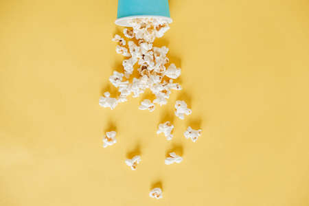 Popcorn in a blue paper cup scattered on a yellow background. Minimalist concept. Top view. Copy, empty space for text.の写真素材
