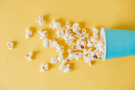 Popcorn in a blue paper cup scattered on a yellow background. Minimalist concept. Top view. Copy, empty space for text.の写真素材