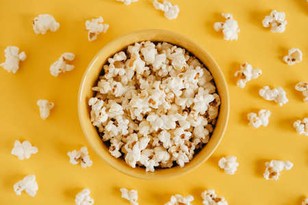 Popcorn in a yellow bowl on a yellow background. Top view. Copy, empty space for text.の写真素材