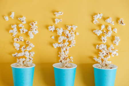 Popcorn in blue paper cups scattered on a yellow background. Top view. Copy, empty space for text.の写真素材