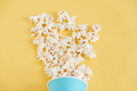 Popcorn in a blue paper cup scattered on a yellow background. Minimalist concept. Top view. Copy, empty space for text.の写真素材
