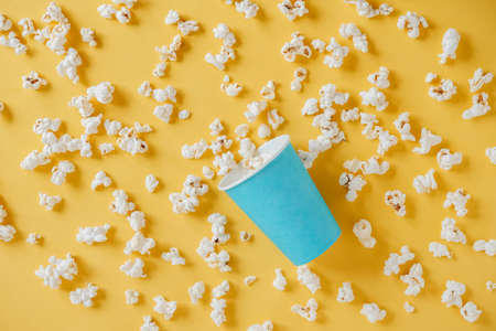 Popcorn in a blue paper cup scattered on a yellow background. Minimalist concept. Top view. Copy, empty space for text.の写真素材