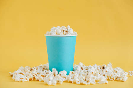 Popcorn in a blue paper cup on a yellow background. Minimalist concept. Copy, empty space for text.の写真素材