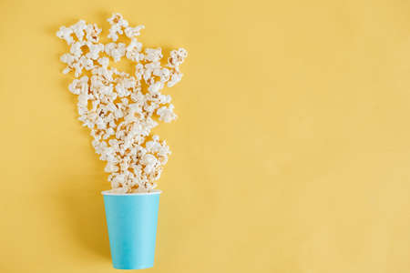 Popcorn in a blue paper cup scattered on a yellow background. Minimalist concept. Top view. Copy, empty space for text.の写真素材