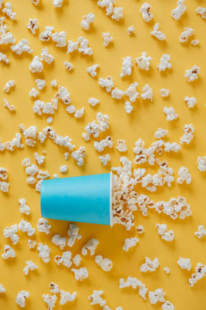 Popcorn in a blue paper cup scattered on a yellow background. Minimalist concept. Top view. Copy, empty space for text.の写真素材
