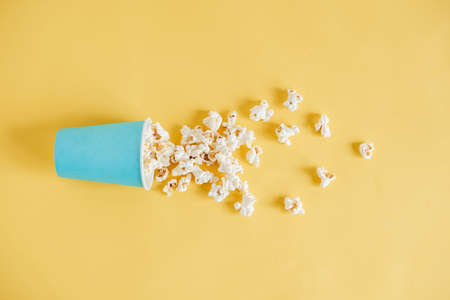 Popcorn in a blue paper cup scattered on a yellow background. Minimalist concept. Top view. Copy, empty space for text.の写真素材