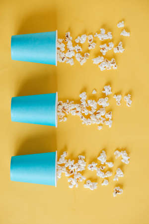 Popcorn in blue paper cups scattered on a yellow background. Top view. Copy, empty space for text.の写真素材