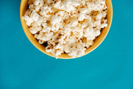 Popcorn in a yellow bowl on a blue background. Top view. Copy, empty space for text.の写真素材