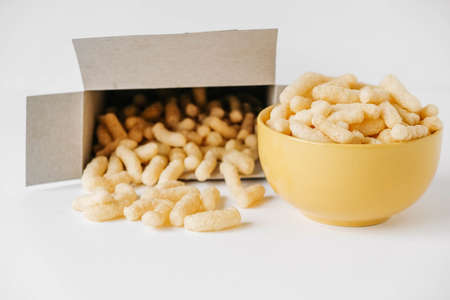 Corn sticks in a yellow bowl and paper box scattered on a white background. Top view. Place for your text.の写真素材