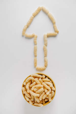 Corn sticks in a yellow bowl scattered in the shape of an pointer on a white background. Top view. Place for your text.の写真素材