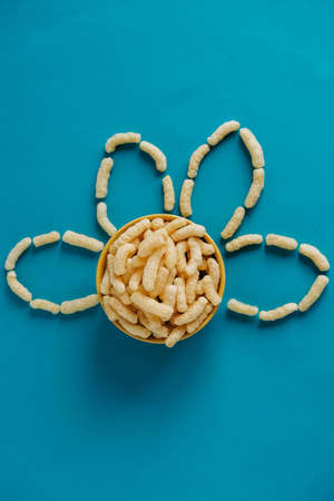Corn sticks in a bowl in the shape of a flower on a blue background. Top view. Place for your text.の写真素材