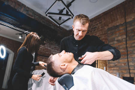 Young male barber makes a haircut beard client with vintage straight razor. Shaving process of beards in Barbershop.の写真素材
