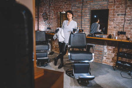 Young beautiful hairdresser woman with scissors in hand against a brick wall background. Barbershop advertising concept. Place for text or advertising.の写真素材