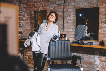 Young beautiful hairdresser woman with scissors in hand against a brick wall background. Barbershop advertising concept. Place for text or advertising.の写真素材