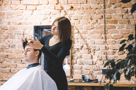 Beautiful female hairdresser cutting client's hair with scissors in a barber shop. Concept of advertising and hairdressing.の写真素材