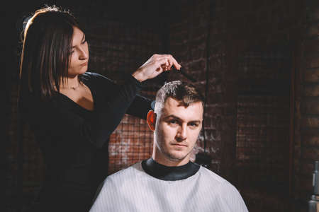 Beautiful female hairdresser cutting client's hair with scissors in a barber shop. Concept of advertising and hairdressing.の写真素材