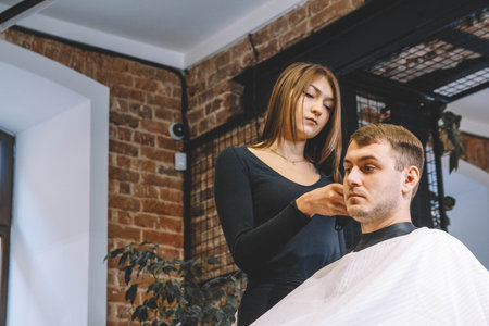 Beautiful female hairdresser cutting client's hair with scissors in a barber shop. Concept of advertising and hairdressing.の写真素材