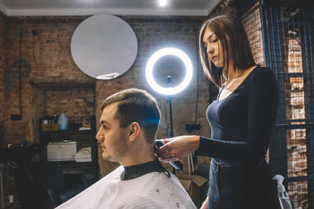 Beautiful female hairdresser cutting client's hair with scissors in a barber shop. Concept of advertising and hairdressing.の写真素材
