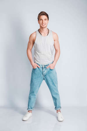Young muscular man in a light T-shirt and black jeans on a white background. Copy, empty space for text.の写真素材