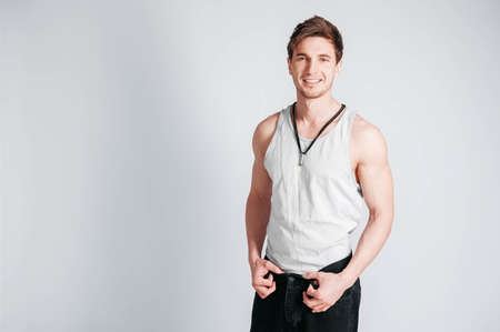 Young muscular man in a light T-shirt and black jeans on a white background. Copy, empty space for text.の写真素材