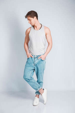 Young muscular man in a light T-shirt and black jeans on a white background. Copy, empty space for text.の写真素材